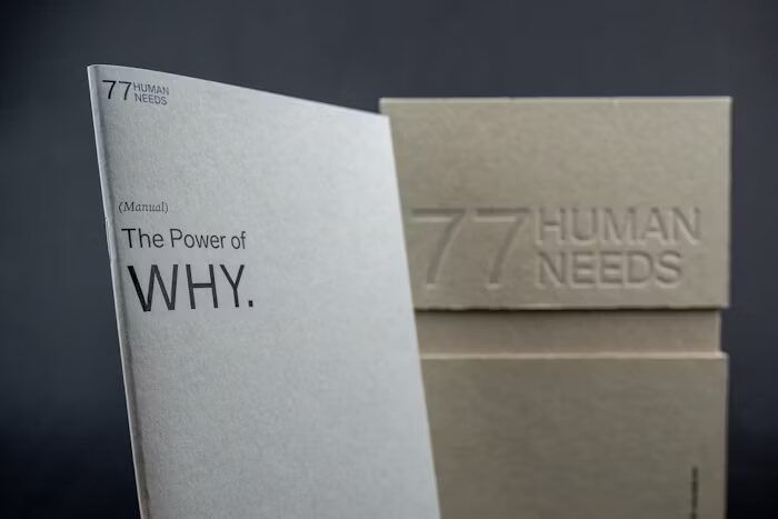 Brosur 'The Power of WHY' dan kotak kardus bertuliskan '77 Human Needs'.