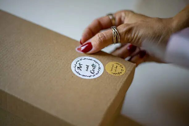 Tangan memegang stiker dan menempelkannya pada kotak kraft.