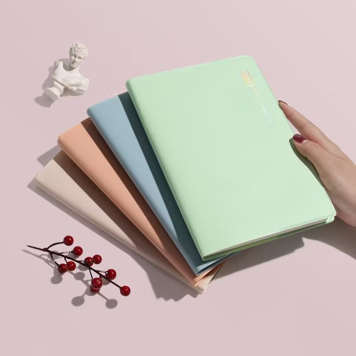 Tumpukan buku hardcover berwarna pastel dengan tangan memegang satu buku.