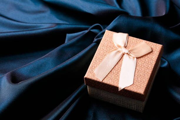 Kotak hadiah kecil dengan pita di atas kain biru sebagai inspirasi kemasan bridesmaid yang rapi dan personal.