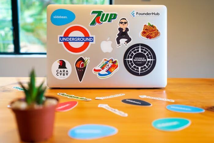 Laptop dengan berbagai stiker desain modern dan unik, termasuk 7UP, Underground, dan lainnya.
