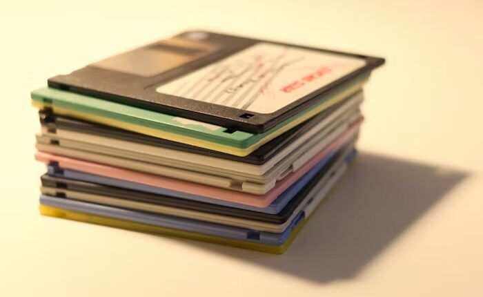 Pile of vintage floppy disks in various colors on a light background.