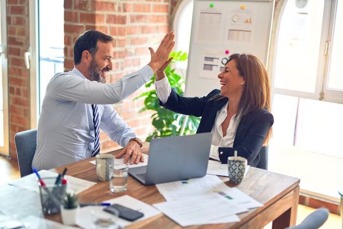 Dua orang sedang high-five di meja kerja kantor modern, menggambarkan proses konsultasi dan order kalender meja custom yang lebih mudah.