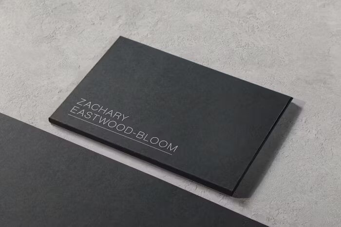 Buku hitam dengan judul 'Zachary Eastwood-Bloom' di atas meja abu-abu.