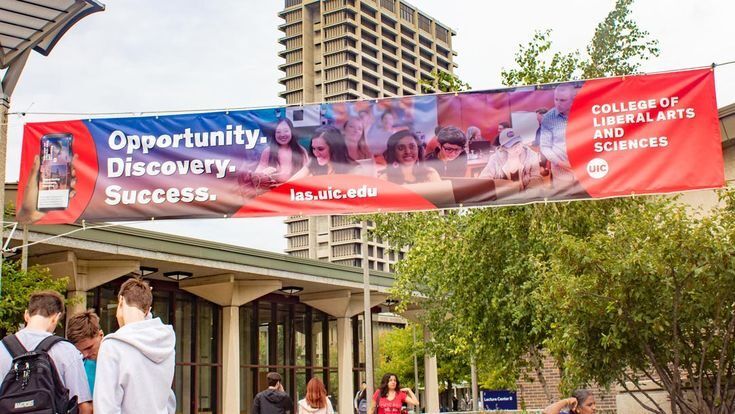 Banner merah dan biru dengan slogan 'Opportunity. Discovery. Success.' di depan gedung universitas.