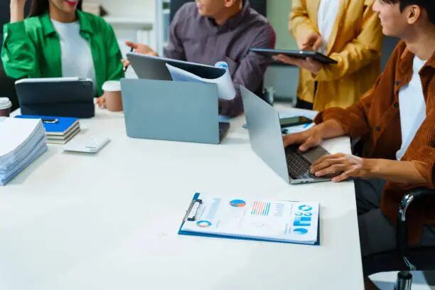 Tim kerja sedang bekerja di meja dengan laptop dan dokumen di Uprint.id