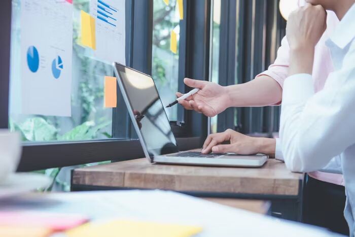 Tiga orang sedang bekerja di kantor dengan laptop dan dokumen.