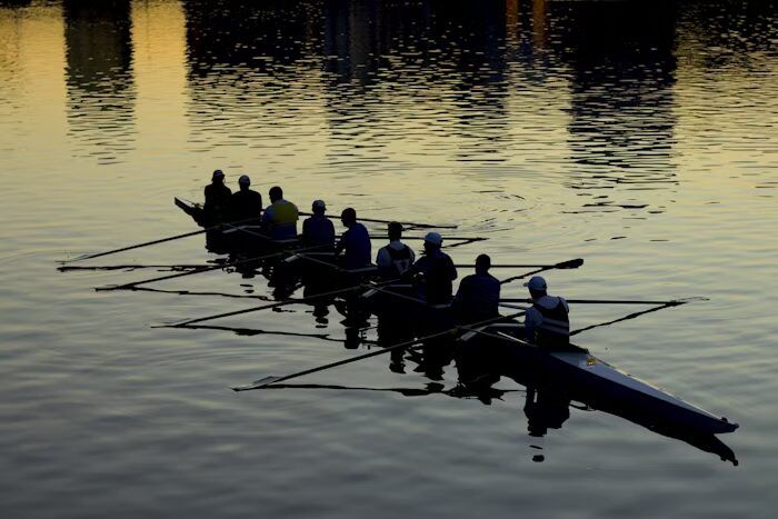 Gambar siluet tim rowing di sungai dengan oars dan refleksi cahaya matahari