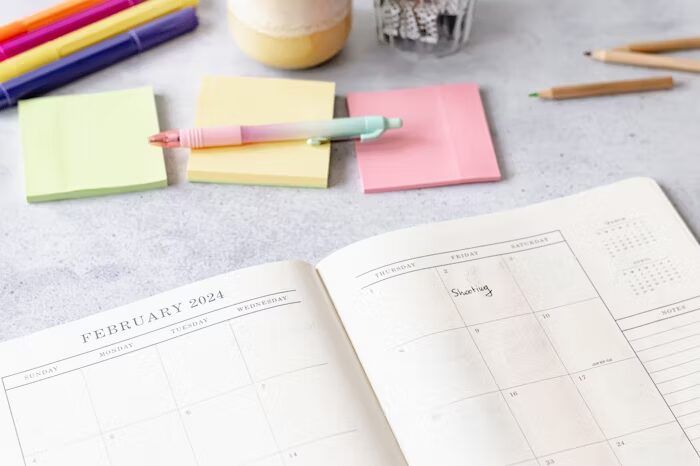 Kalender bulan Februari 2024 dengan sticky notes berwarna-warni dan alat tulis di meja kerja.