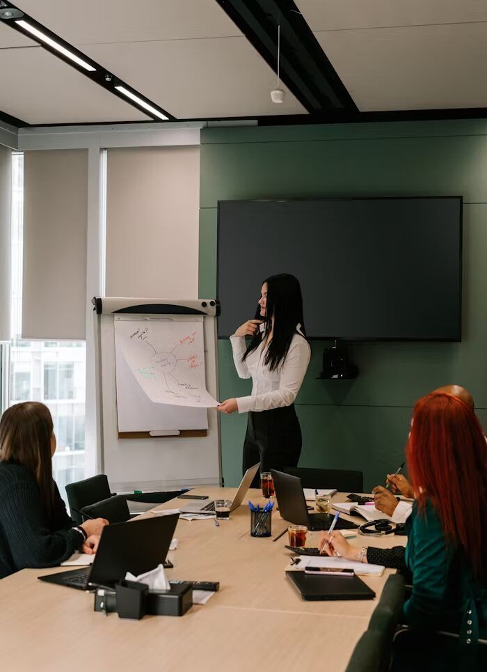Grafik presentasi di flipchart dan laptop di meja rapat.