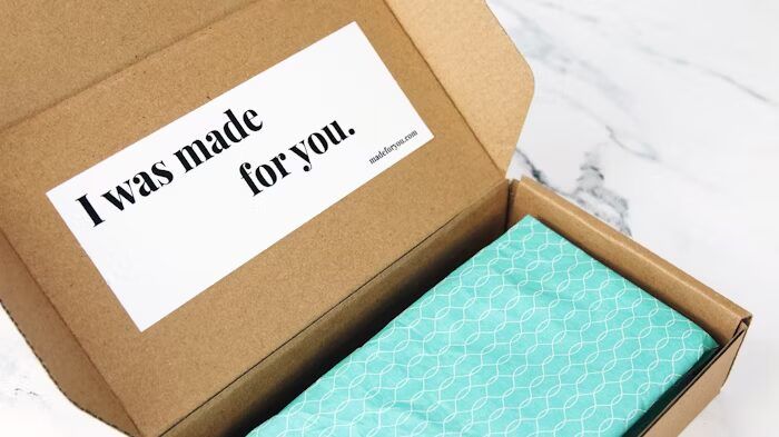 Kotak karton dengan stiker 'I was made for you' dan kertas biru dengan motif geometris.