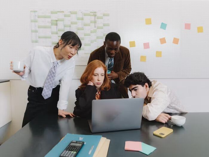Empat orang sedang bekerja sama dengan laptop di meja kantor.