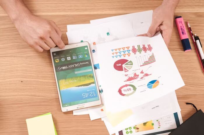 Tangan memegang tablet dan dokumen grafik di meja percetakan