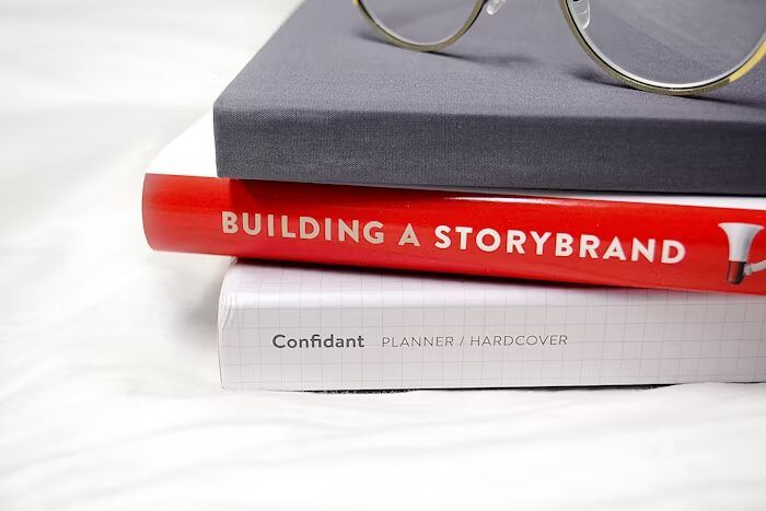 Buku 'Building a Storybrand' dan agenda 'Confidant Planner' di atas kacamata.