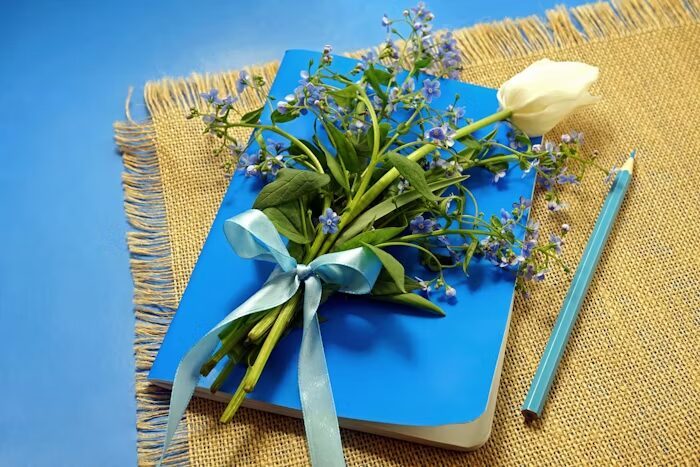 Buku biru dengan bunga kecil dan pensil biru di atas kain jute.