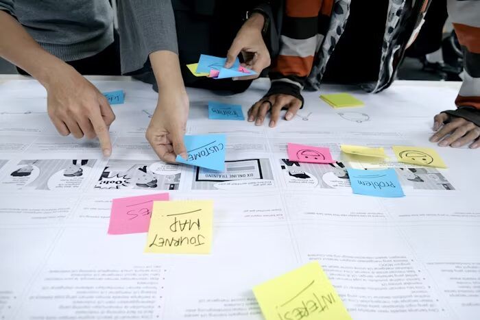 Tangan orang-orang menempelkan sticky notes berwarna-warni pada lembaran dokumen untuk review file booklet sebelum order online
