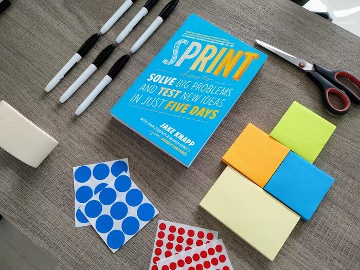 Buku 'Sprint' dan stiker biru, warna-warni, pensil, dan剪刀。