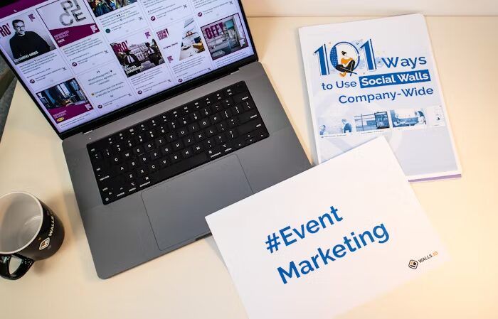 Buku '101 Ways to Use Social Walls' dan poster '#Event Marketing' di depan laptop.