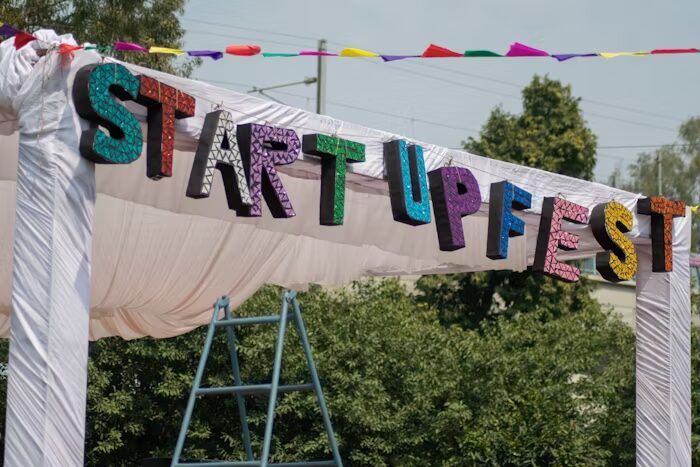 Bendera berwarna-warni bertuliskan STARTUPFEST di depan latar hijau alam