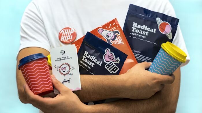 Tangan memegang paket kopi 'Radical Toast' dan aksesori minum.