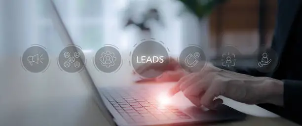 Tangan mengetik di laptop dengan ikon leads dan alat digital di sekitarnya.