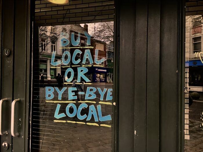 Teks Buy Local or Bye-Bye Local pada kaca toko sebagai visual promosi untuk materi cetak bisnis