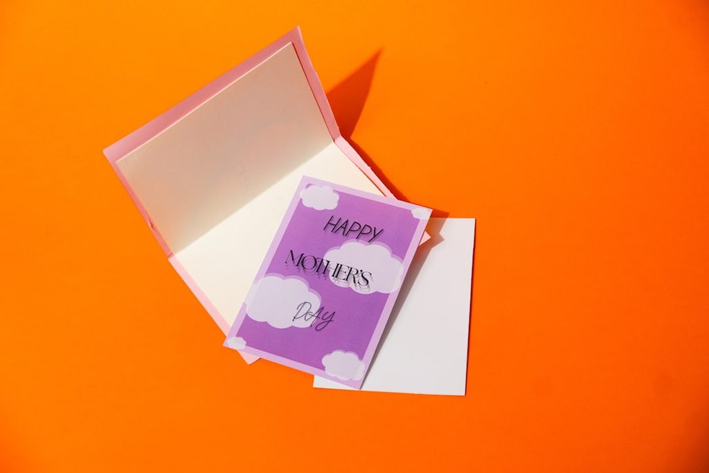 Gambarkan kartu ucapan 'Happy Mother's Day' dengan warna ungu dan putih, bersama dengan kotak kertas