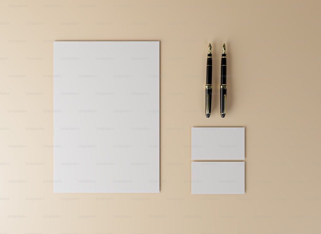 Gambar menunjukkan mockup kertas, pena, dan kartu nama di atas permukaan pastel.