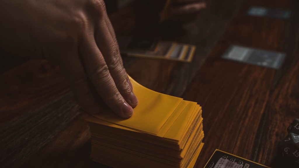 Tangan memegang beberapa lembar kertas kuning di atas meja kayu.