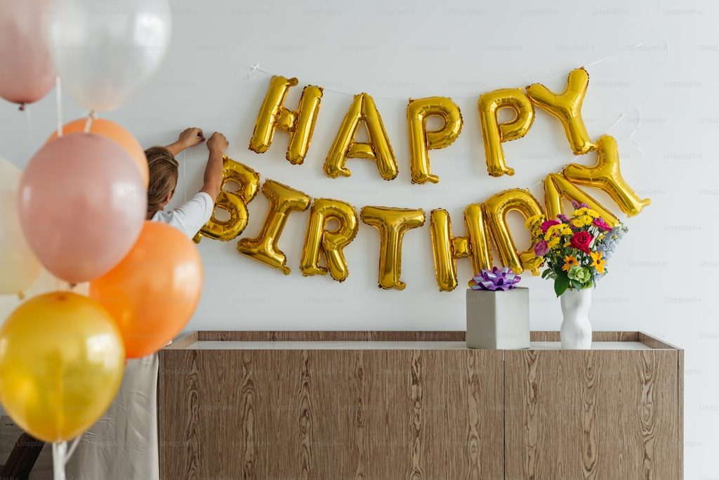 Gambar dekorasi ulang tahun dengan balon HAPPY BIRTHDAY dan bunga mawar di meja kayu.