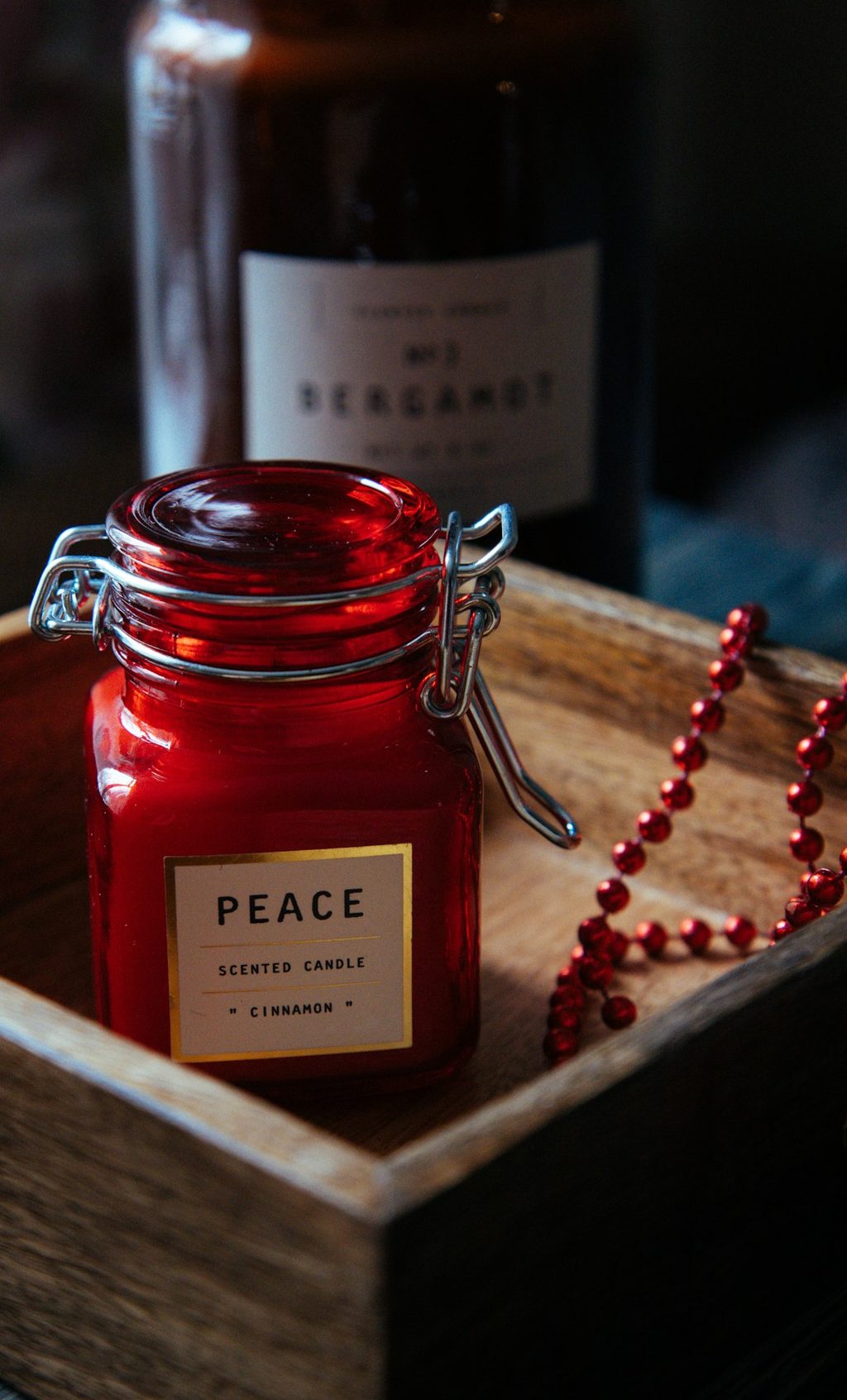 Kerajinan lilin aromaterapi merah dengan label 'Peace' dan kalung merah di meja kayu.