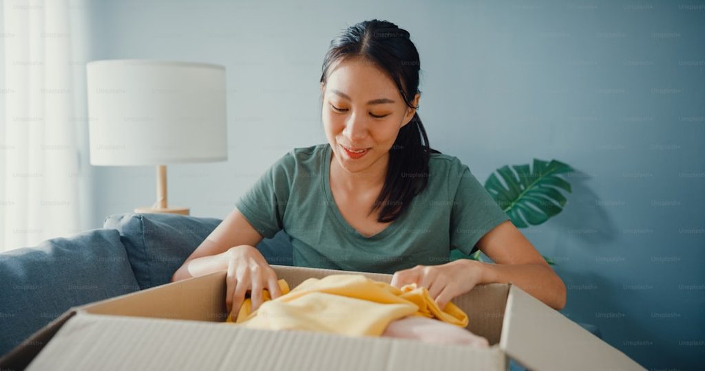 Perempuan membuka kotak berisi baju kuning di ruang tamu.