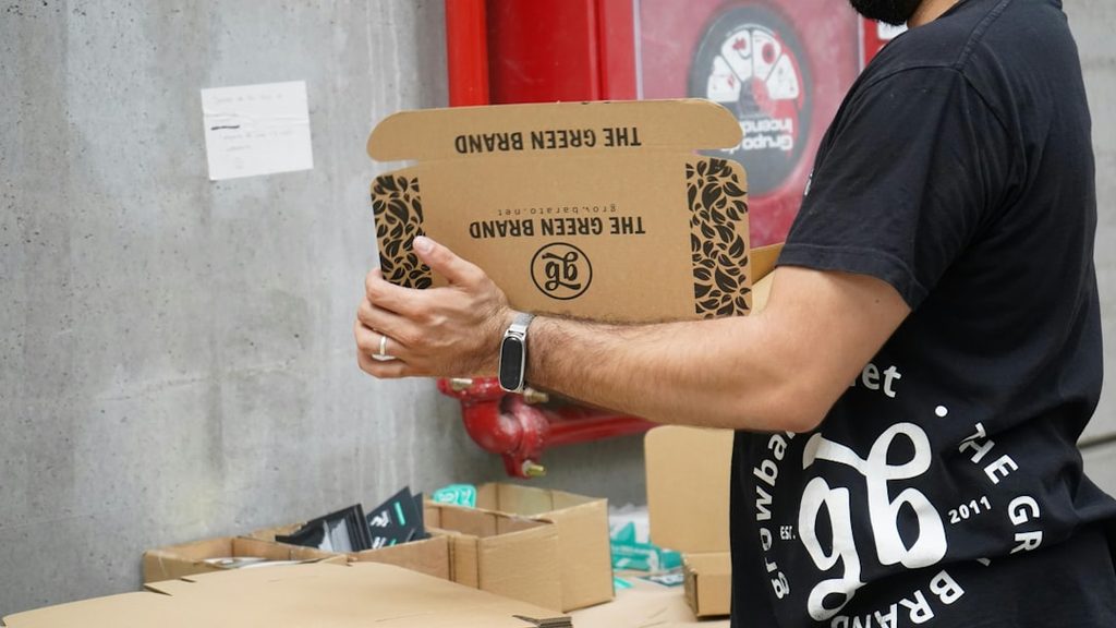 Man holding a cardboard box with leopard print design and 'The Green Brand' text.