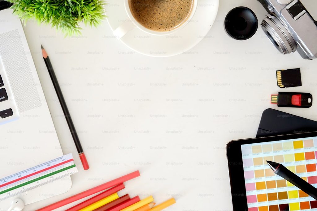 Workspace setup featuring color swatches, stationery, and a digital tablet on a white background.