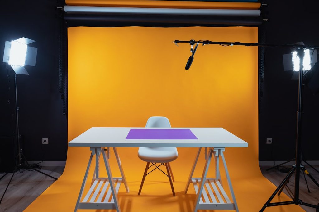Meja dan kursi di studio fotografi dengan background kuning dan lampu profesional.