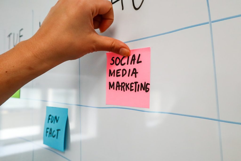 Tangan menempelkan stiker merah dengan tulisan 'SOCIAL MEDIA MARKETING' di whiteboard.