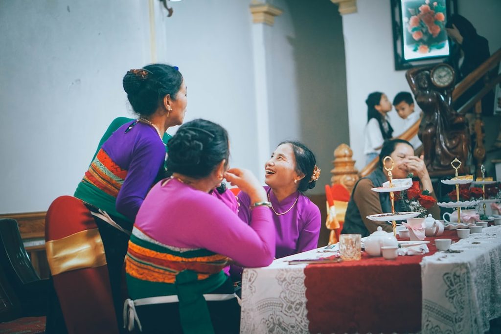 Tiga orang perempuan merayakan ulang tahun di restoran dengan piring makanan dan minuman.