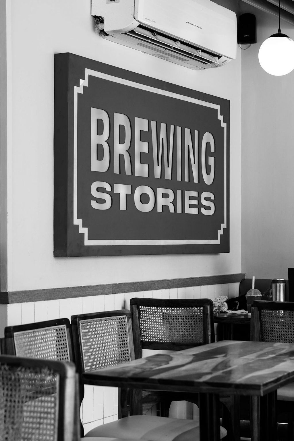 Gambar hitam putih papan iklan 'Brewing Stories' di dinding kafe.