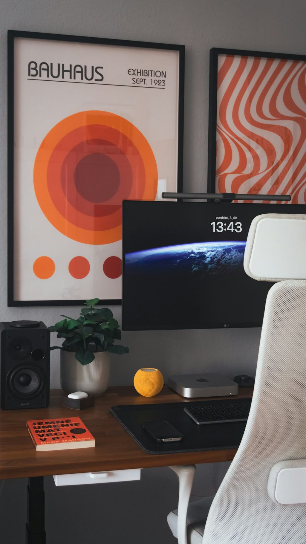 Workspace modern dengan monitor, kursi ergonomis, dan poster Bauhaus di dinding.