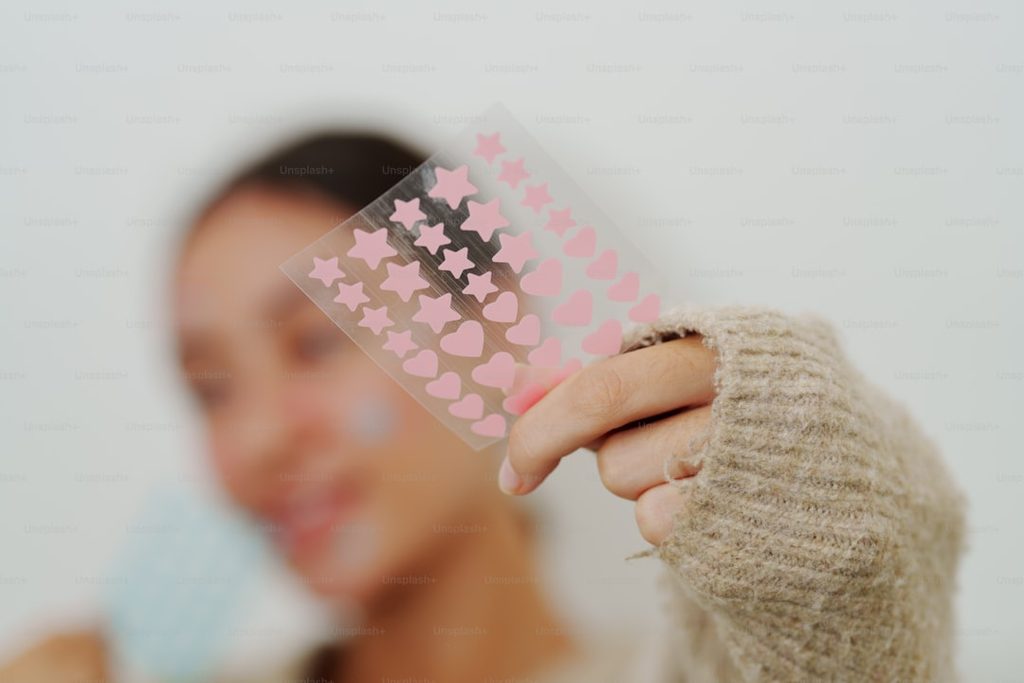 Tangan memegang stiker berbentuk hati warna pink.