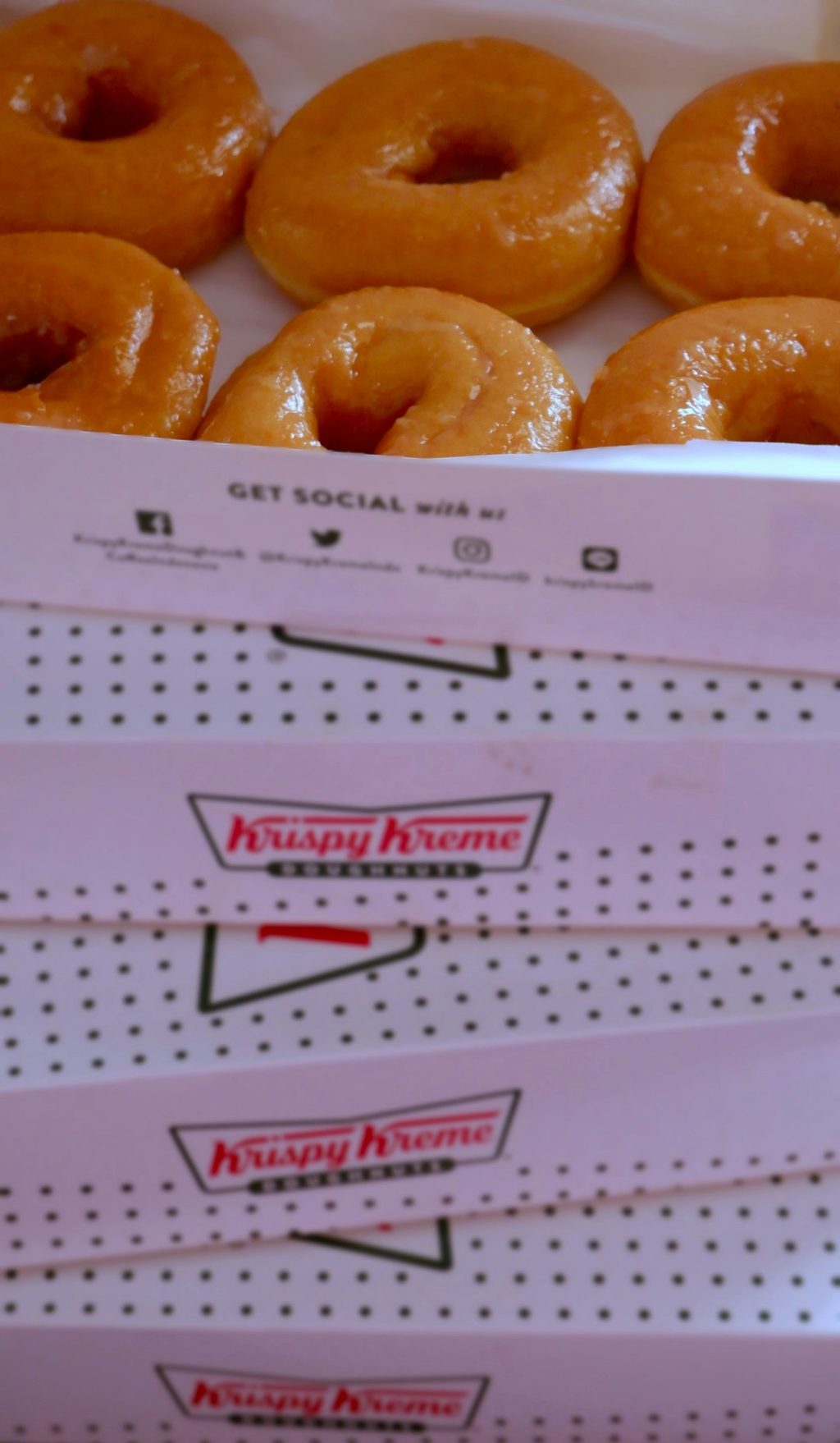 Krispy Kreme donuts arranged neatly in a box with branding.