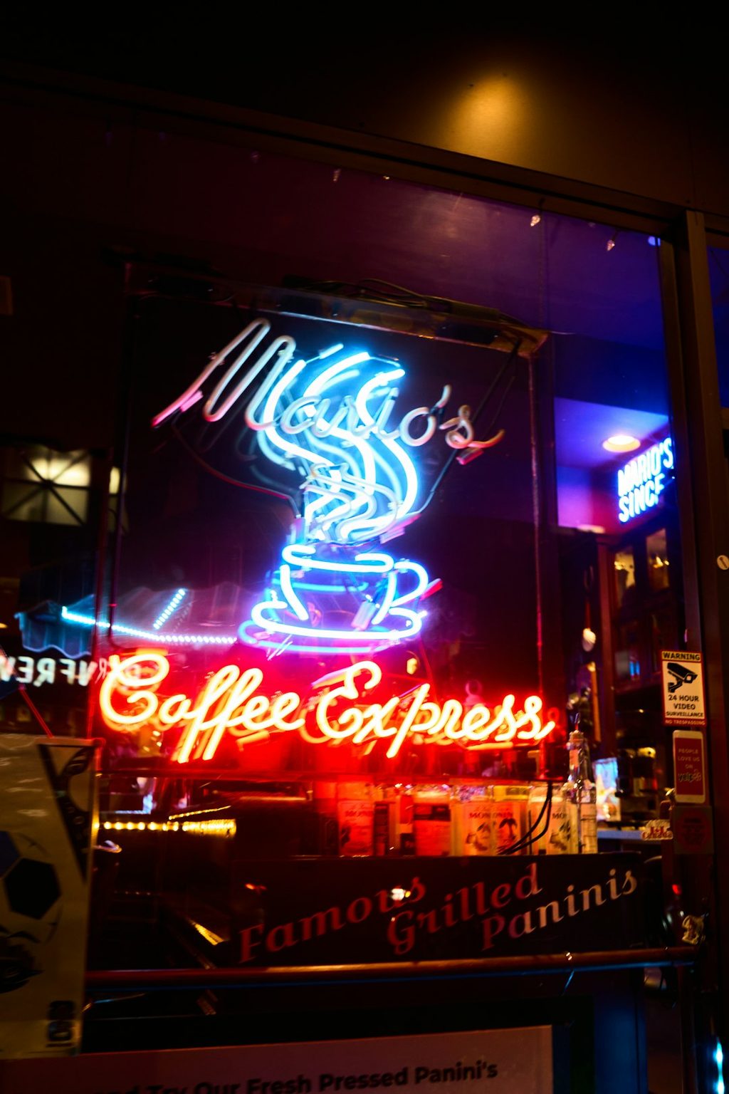 Tanda neon Coffee Express dengan gambar cangkir kopi dan tulisan merah di kaca toko.