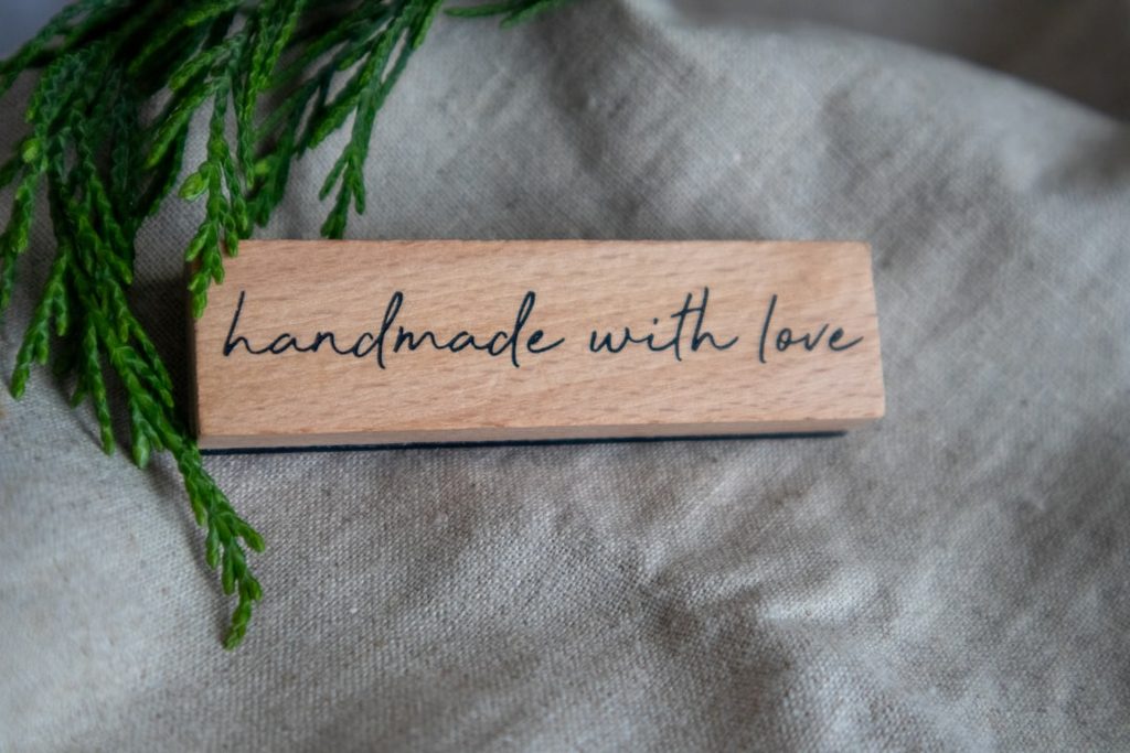 Plaque kayu dengan tulisan 'handmade with love' di atas latar belakang hijau alami.