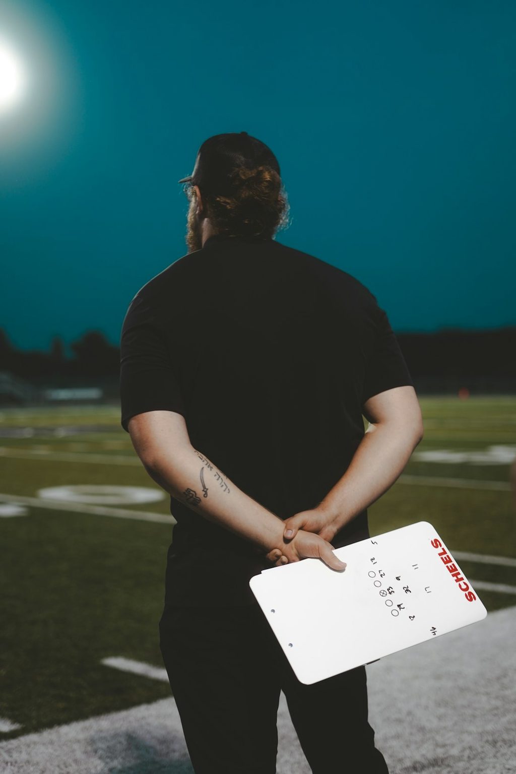 Pelatih sepak bola memegang daftar strategi di lapangan malam hari sebagai analogi strategi distribusi flyer