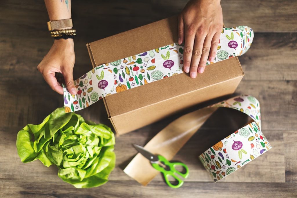 Tangan membalut kotak hadiah dengan wrapping paper berwarna-warni untuk menciptakan kesan premium.