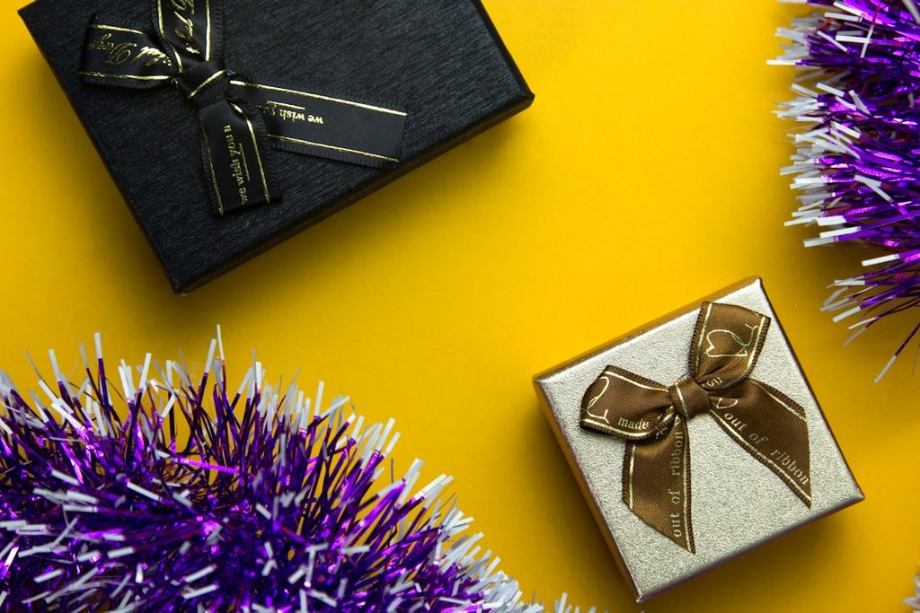 Paket hadiah natal dengan kotak kemasan elegan dan tinsel ungu.