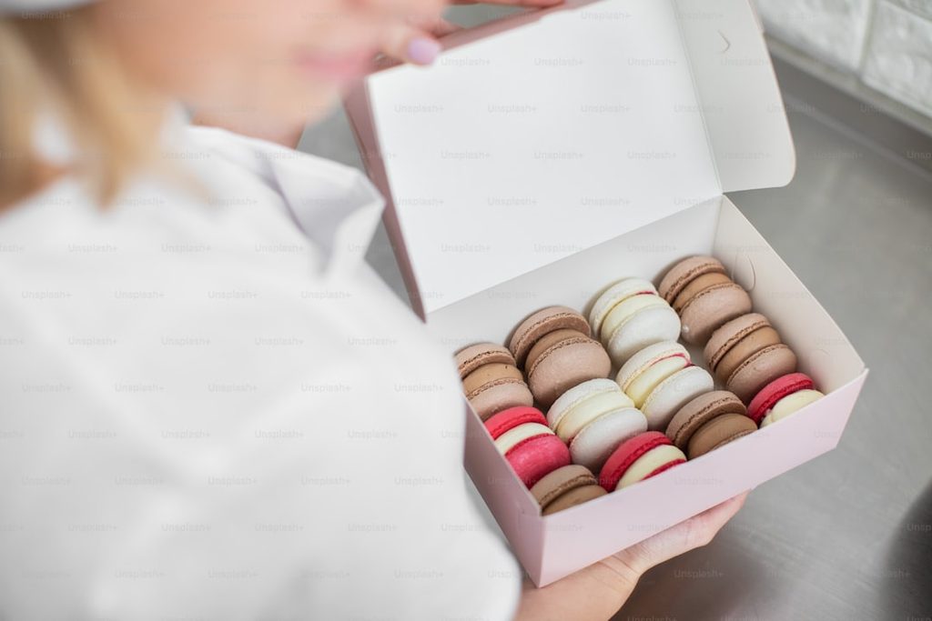 Tangan memegang kotak berisi macaron warna-warni