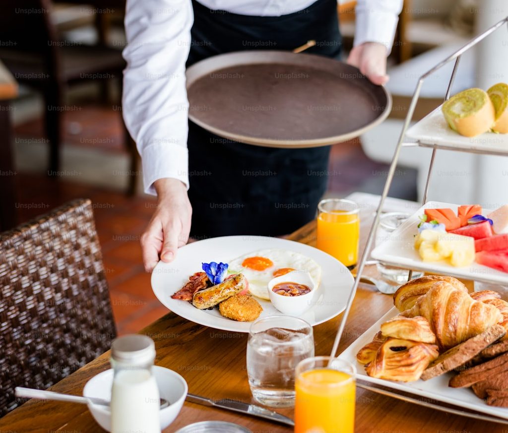 Waiter presenting a tray of breakfast items on a wooden table.