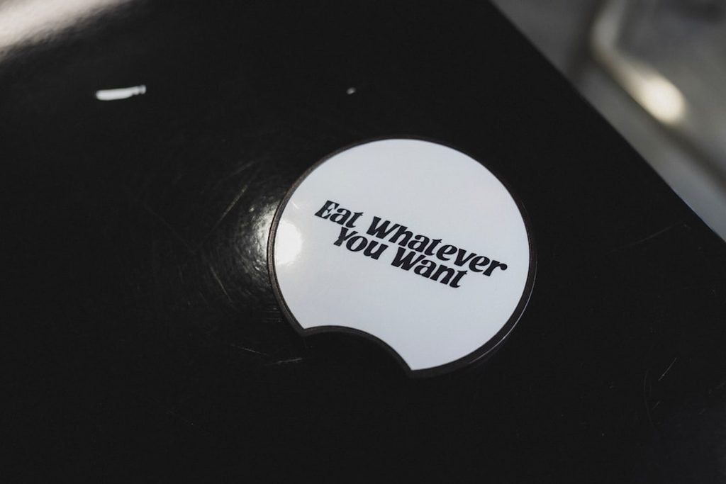 Stiker putih bertuliskan pesan singkat di atas permukaan hitam, menunjukkan pentingnya tipografi yang jelas pada label dan materi promosi kecil.