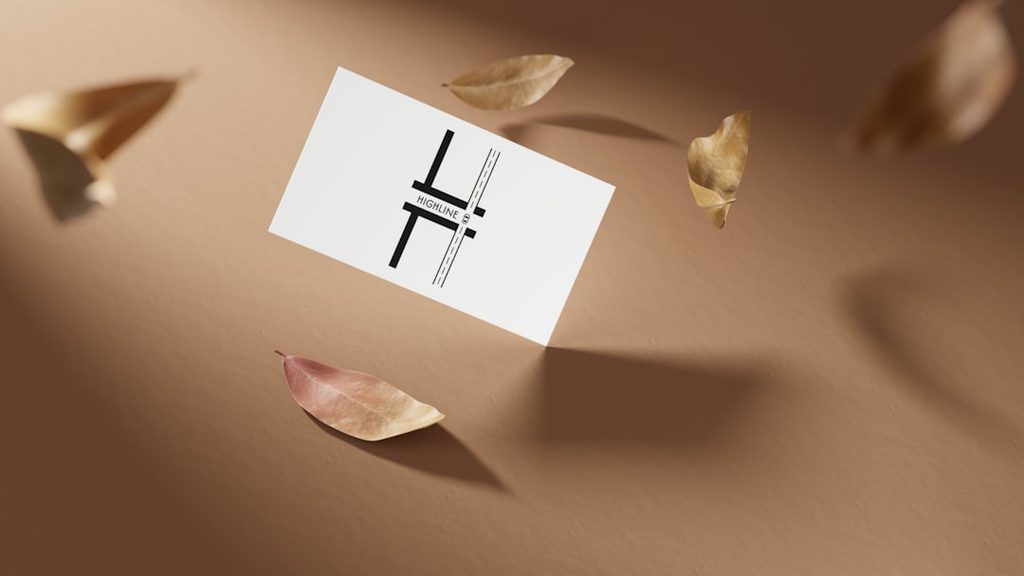 Mockup kartu nama putih dengan logo hitam, latar belakang coklat dan daun kering.